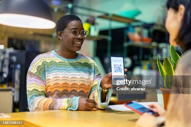 african woman showing qr code on her phone to the receptionist at makers space - diversity showcase arrivals stock pictures, royalty-free photos & images