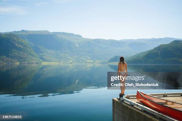 woman standing near the lake in swimsuit near red canoe - morning swim stockfoto's en -beelden