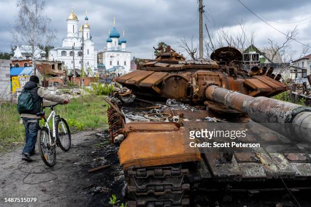 Cyclist passes a destroyed Russian tank that lies near the Cathedral of Saints Vera, Nadeshda and Liubov, an Orthodox Church loyal to the Moscow...