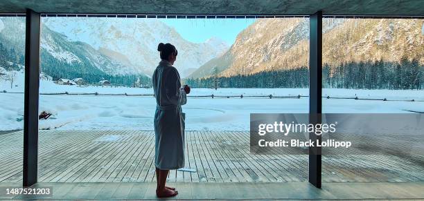una donna in una spa che tiene in mano una tazza con vista invernale sulle montagne. - sauna winter foto e immagini stock