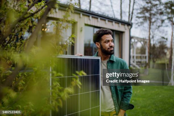 portrait of young man with solar panel standing in front of house. - eco house stockfoto's en -beelden