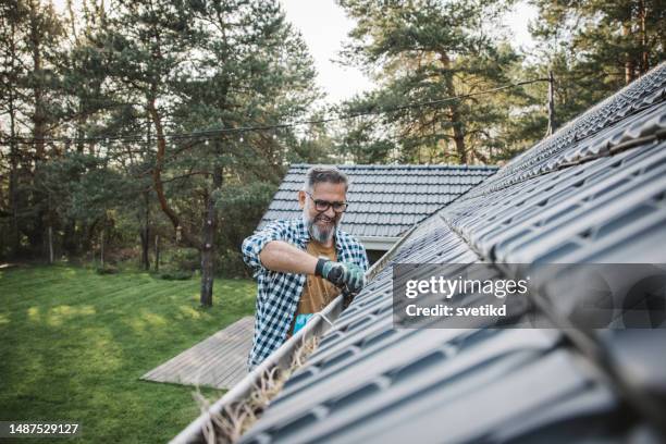 mann reinigt blätter von der dachrinne des hauses - gutter stock-fotos und bilder