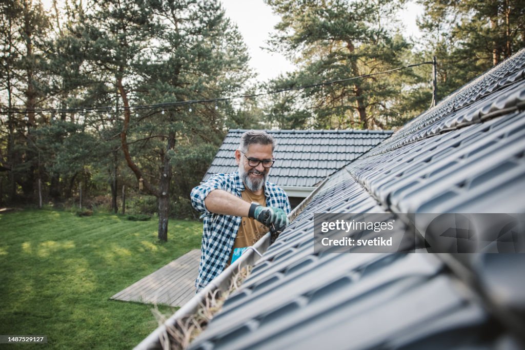 Man cleaning leaves from guttering of house