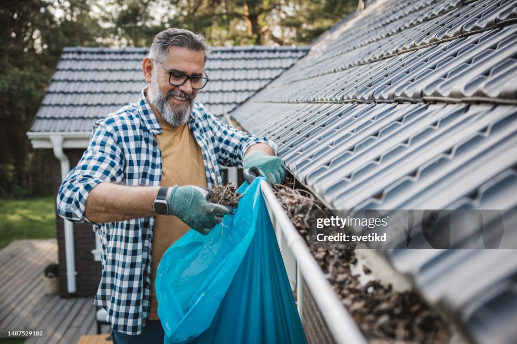 Man cleaning leaves from guttering of house