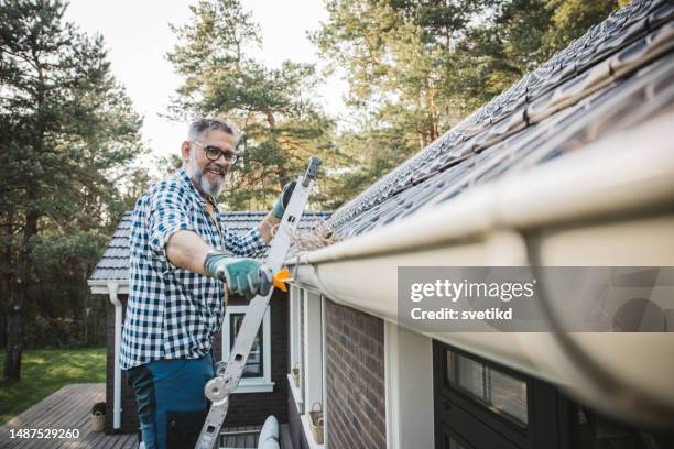 man cleaning leaves from guttering of house - cleaning gutters stock pictures, royalty-free photos & images