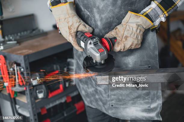 nahaufnahme von handwerkerhänden, die metall schneiden und winkelschleifer in der heimischen werkstatt verwenden - schutzhandschuh stock-fotos und bilder