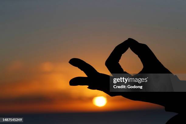 Woman practising yoga meditation by the sea at sunset as concept for silence and relaxation. Close-up on hand, gyan mudra.