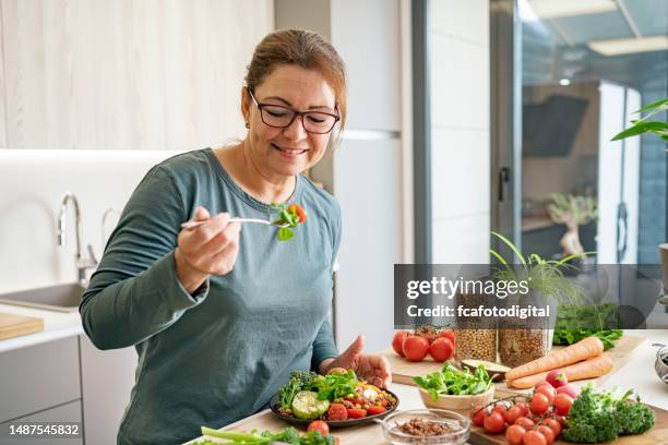 mujer degustando ensalada vegana saludable en casa - dieta a base de plantas fotografías e imágenes de stock