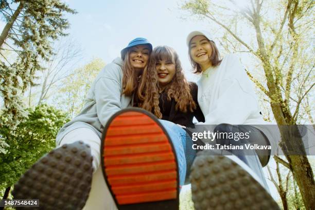 three female college friends taking silly pictures holding their shoes soles above camera lying on ground - woman soles stockfoto's en -beelden