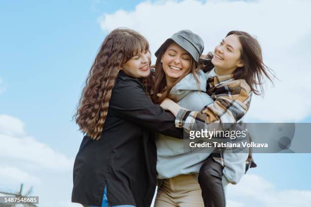 happy young women in casual clothes having group hug laughing with blue sky in background - blue sky friends photos et images de collection