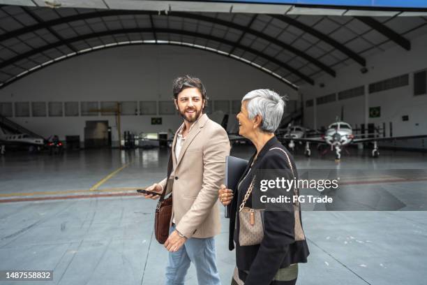 compañeros de trabajo hablando mientras caminan en el hangar del aeropuerto - hangar fotografías e imágenes de stock