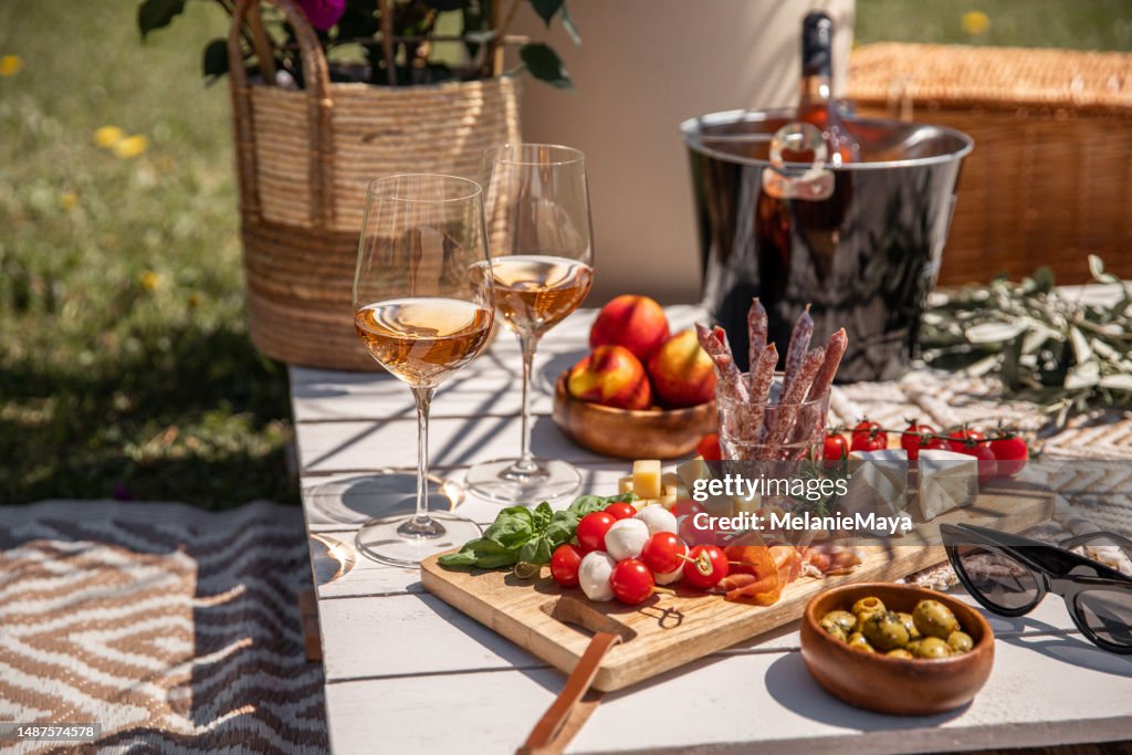 Bicchieri di vino rosa con antipasti spuntini da picnic sul tavolo soleggiato della festa del giardino