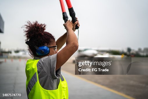 Woman signaling the pilot with marshalling wands on airport