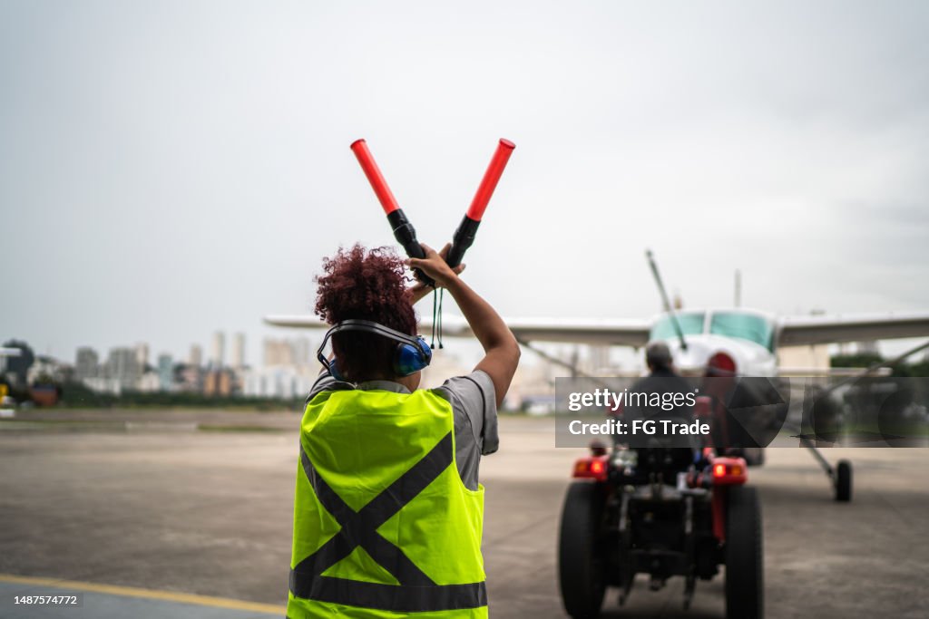 Femme signalant le pilote avec des baguettes de triage à l’aéroport