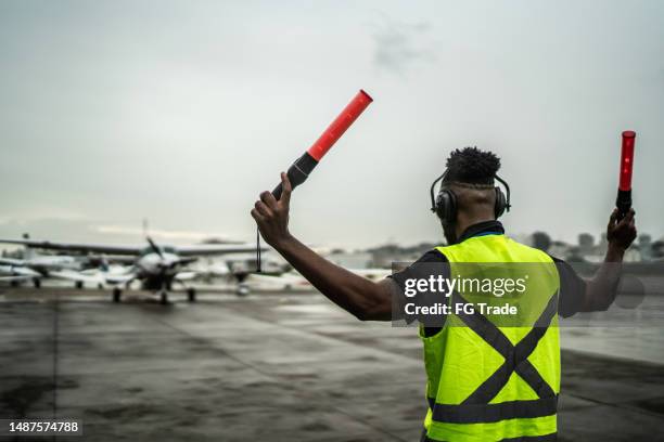 man signaling the pilot with marshalling wands on airport - airport tarmac stock pictures, royalty-free photos & images
