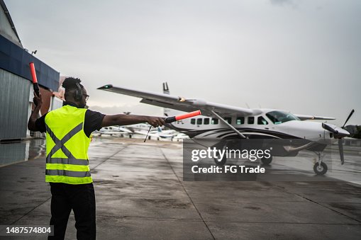 Man signaling the pilot with marshalling wands on airport