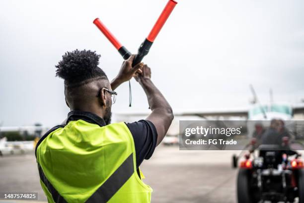 man signaling the pilot with marshalling wands on airport - airport tarmac stock pictures, royalty-free photos & images