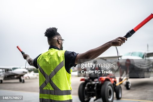 Man signaling the pilot with marshalling wands on airport