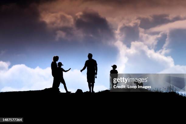 Family and their pet dog seen in silhouette walking in the late evening sunlight on Pentire Point East in Newquay in Cornwall.