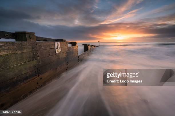 Waves washing around a groyne on a beach at sunrise.