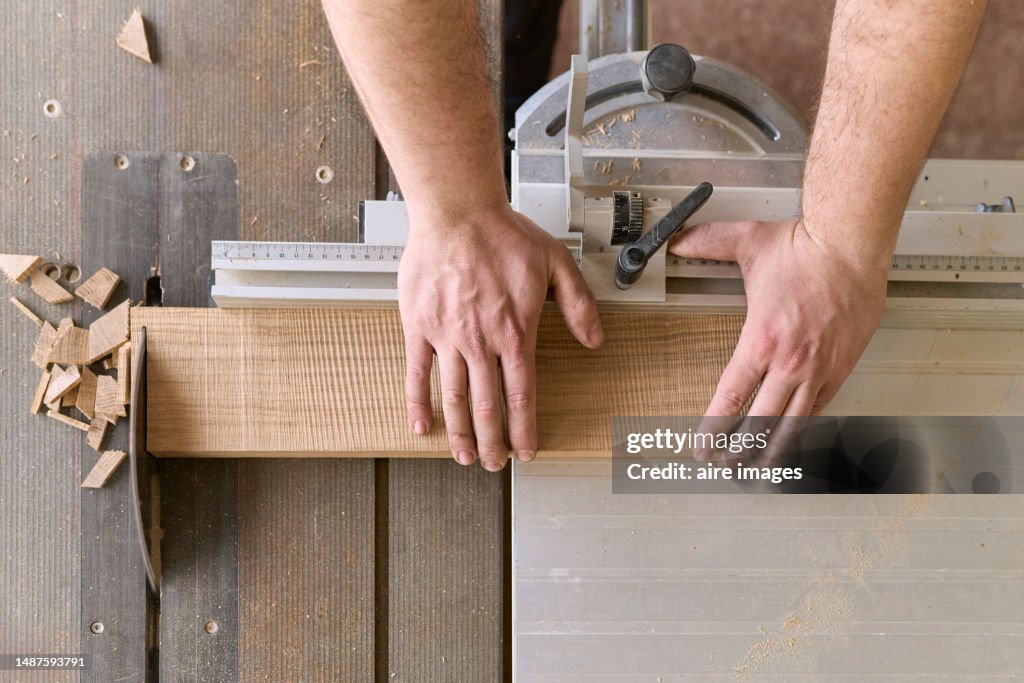 High angle view of a carpenter's hands holding a sheet of wood as he passes it through the circular shop shutter.