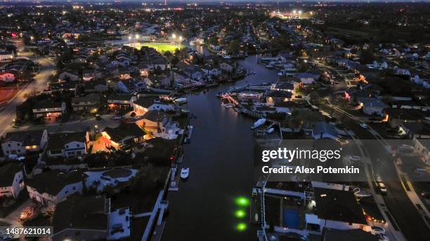 pier with yachts and town on waterfront illuminated in the dark. public community stadium in lights in oceanside, long island. aerial view - nassau aerial stock pictures, royalty-free photos & images