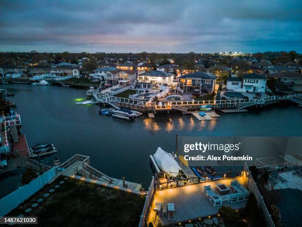 luxury neighborhood with modern houses and yachts by the creek at dusk. small town and pier by water bay in oceanside, long island. aerial view - bedding stockfoto's en -beelden