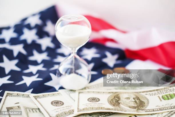 sandglass standing on 100 dollar bills and us flag. - depresión económica fotografías e imágenes de stock