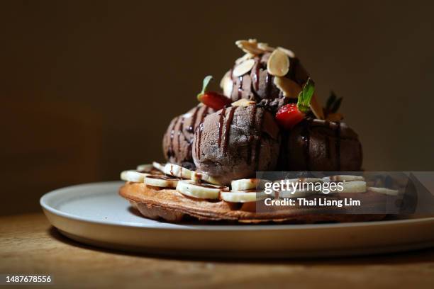 a mouth-watering belgian waffle dessert topped with chocolate ice cream, fresh strawberries and banana slices, and a decadent chocolate drizzle - chocolate drizzle stock pictures, royalty-free photos & images