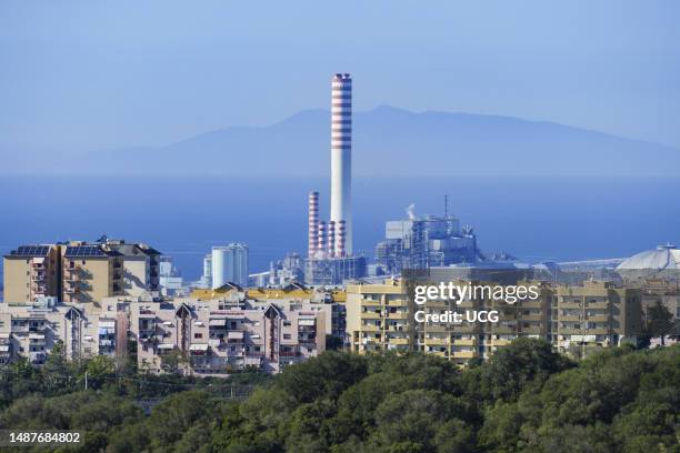 The chimney of the Torrevaldaliga Nord thermoelectric power plant towers above the buildings of Civitavecchia. In the background, lost in the blue...