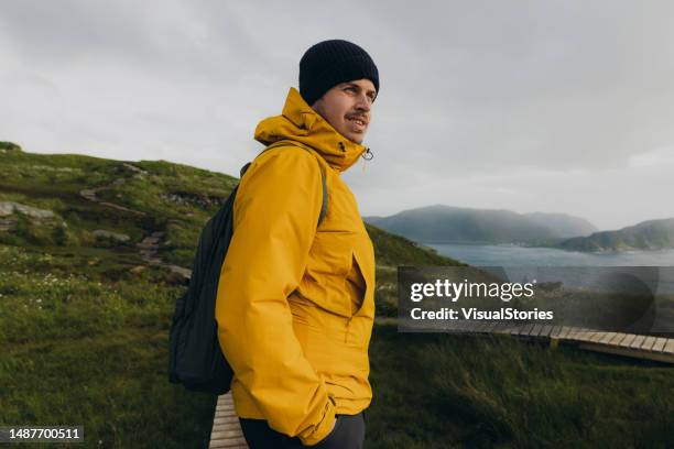 seitenansicht eines rucksacktouristen, der auf der malerischen insel runde in norwegen wandert - gelbe jacke stock-fotos und bilder