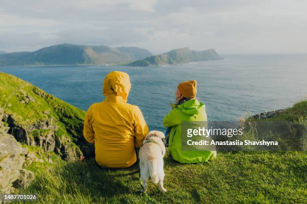 rear view of happy woman and man with dog conteplating sea view on runde island, norway - westelijke fjorden noorwegen stockfoto's en -beelden