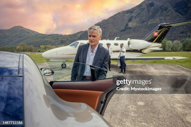 chauffeur opening luxury car door, private jet in the background - commercieel vliegtuig deur stockfoto's en -beelden