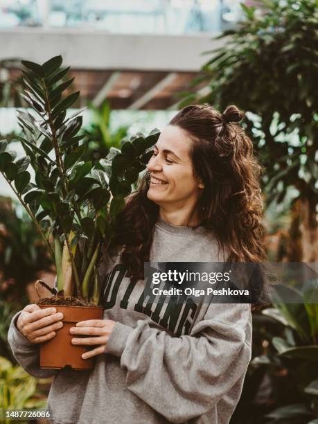 a woman with long dark hair chose a beautiful houseplant in a garden shop - human age stock pictures, royalty-free photos & images
