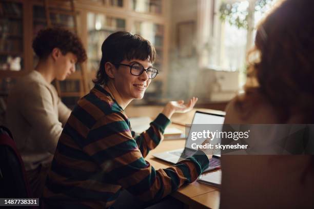 happy female student talking to her friend while studying in library. - boy library stock pictures, royalty-free photos & images