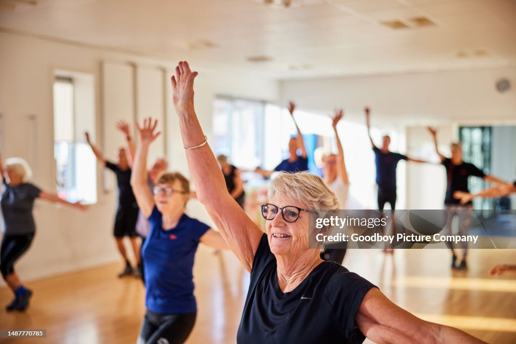 Smiling senior woman and others taking an exercise class at the gym