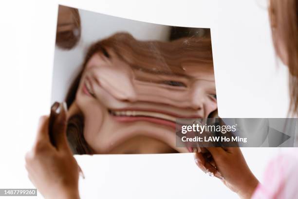 a young woman looks at the distorted mirror in her hand and keeps laughing - verzerrt stock-fotos und bilder