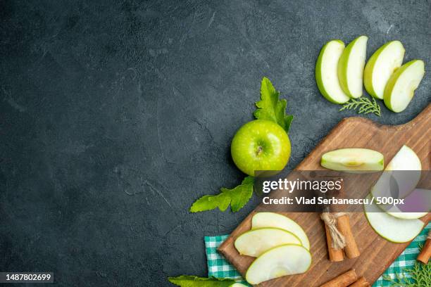 top view apple slices and cinnamon on chopping board dried mint powder in small bowl apple on black background with free space - cutting green apple stock pictures, royalty-free photos & images
