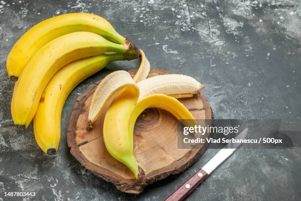 top view nutrition source fresh bananas bundle and peeled on wooden cutting board knife on gray background - plátano fruta tropical fotografías e imágenes de stock