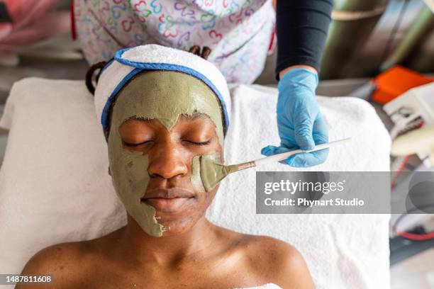 acne facial mask applied to a black woman in a wellness spa center using a special brush - esthetician stock pictures, royalty-free photos & images