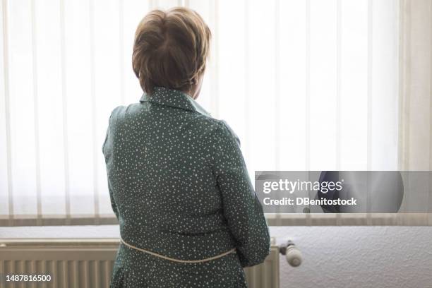 senior lady with alzheimer's and depression, with her back turned, looking thoughtfully out a window. concept of old age, disease, loneliness, forgetfulness and memory. - dementia stock pictures, royalty-free photos & images