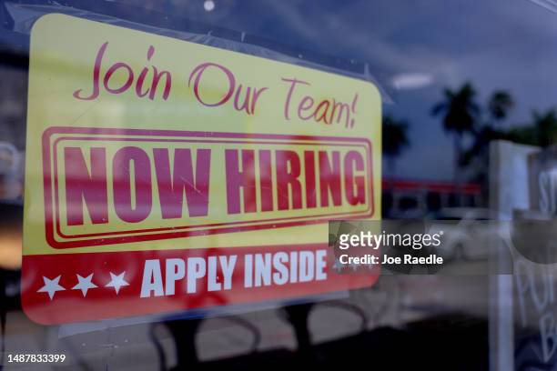 Now Hiring' sign posted in the window of a restaurant looking to hire workers on May 05, 2023 in Miami, Florida. A report by the Bureau of Labor...