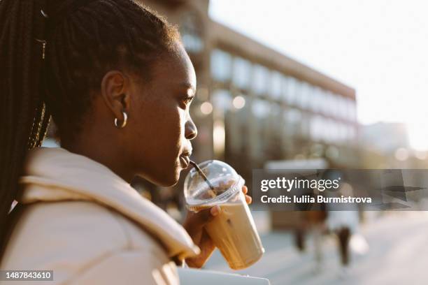 side portrait of young black woman with black braided hair drinking coffee looking away in downtown - braids stock pictures, royalty-free photos & images