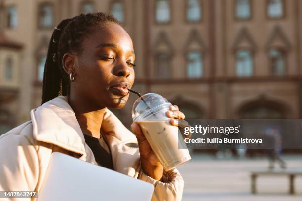 young black blogger drinking ice latte from disposable cup standing in town square - pleased face laptop stock pictures, royalty-free photos & images