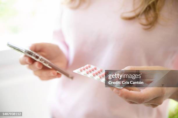 woman holding contraceptive pill and checking smartphone - birth control pill stock pictures, royalty-free photos & images