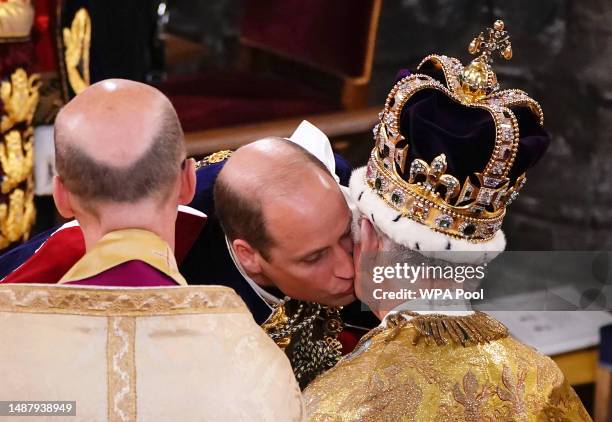 Prince William, Prince of Wales kisses his father, King Charles III, wearing St Edward's Crown, during the King's Coronation Ceremony inside...