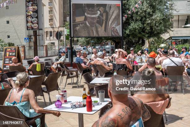 British tourists watch the Coronation of King Charles III and Queen Camila as they sunbath at the terrace of teh Rockstar Benidorm bar on May 06,...