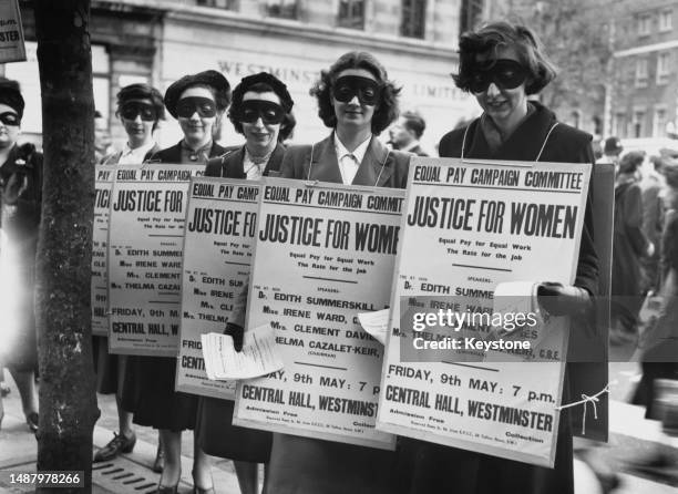 Masked women wearing sandwich boards during a poster parade advertising a meeting advocating equal pay rights for women, at Central Hall in...