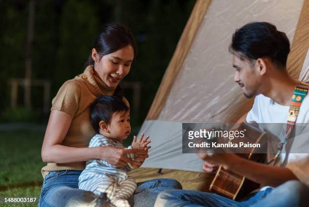 asian family playing guitar and singing during outdoor camping holiday travel in nature. - toddler musical instrument stock pictures, royalty-free photos & images