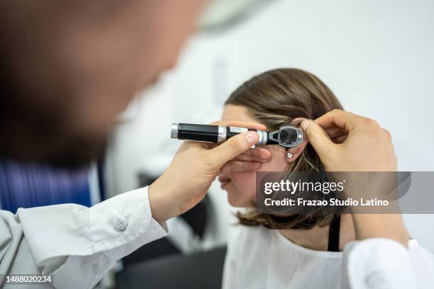 doctor/otolaryngologist using an otoscope in a patient's ear at medical clinic - ear exam stock pictures, royalty-free photos & images